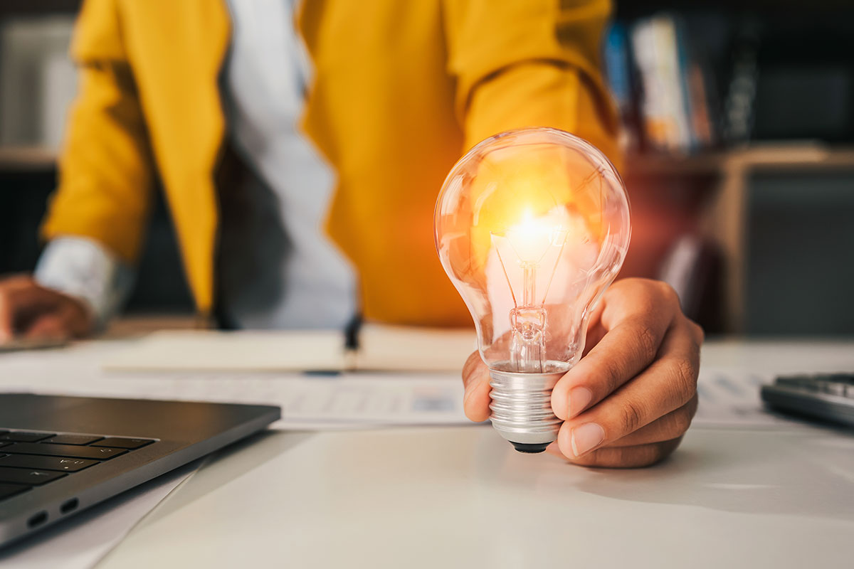 woman holding lit up lightbulb on work desk to represent innovation